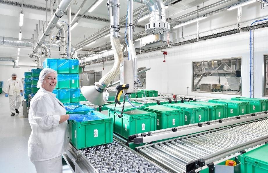 Pracovnice skladu surovin u dopravníku se zelenými přepravkami Hügli